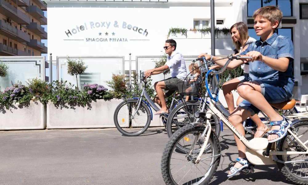 Famiglia che va in bicicletta vicino a un hotel in una giornata di sole.