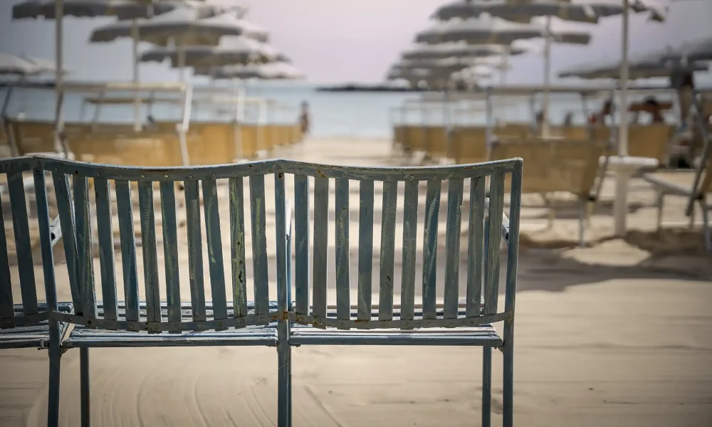 Panchina vuota sulla spiaggia con ombrelloni sfocati sullo sfondo.