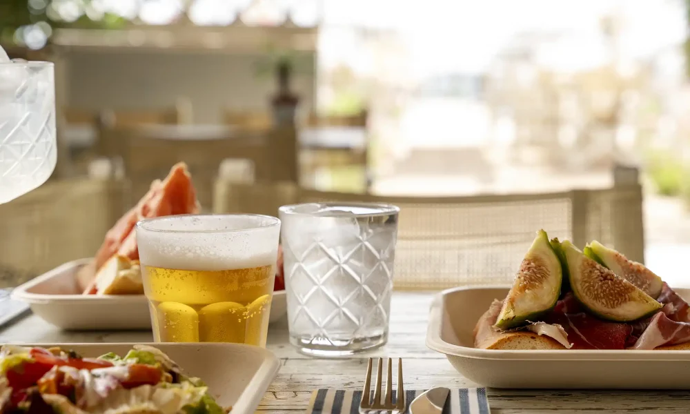 Pranzo estivo con birra, acqua e piatti di fichi e salumi su un tavolo esterno.